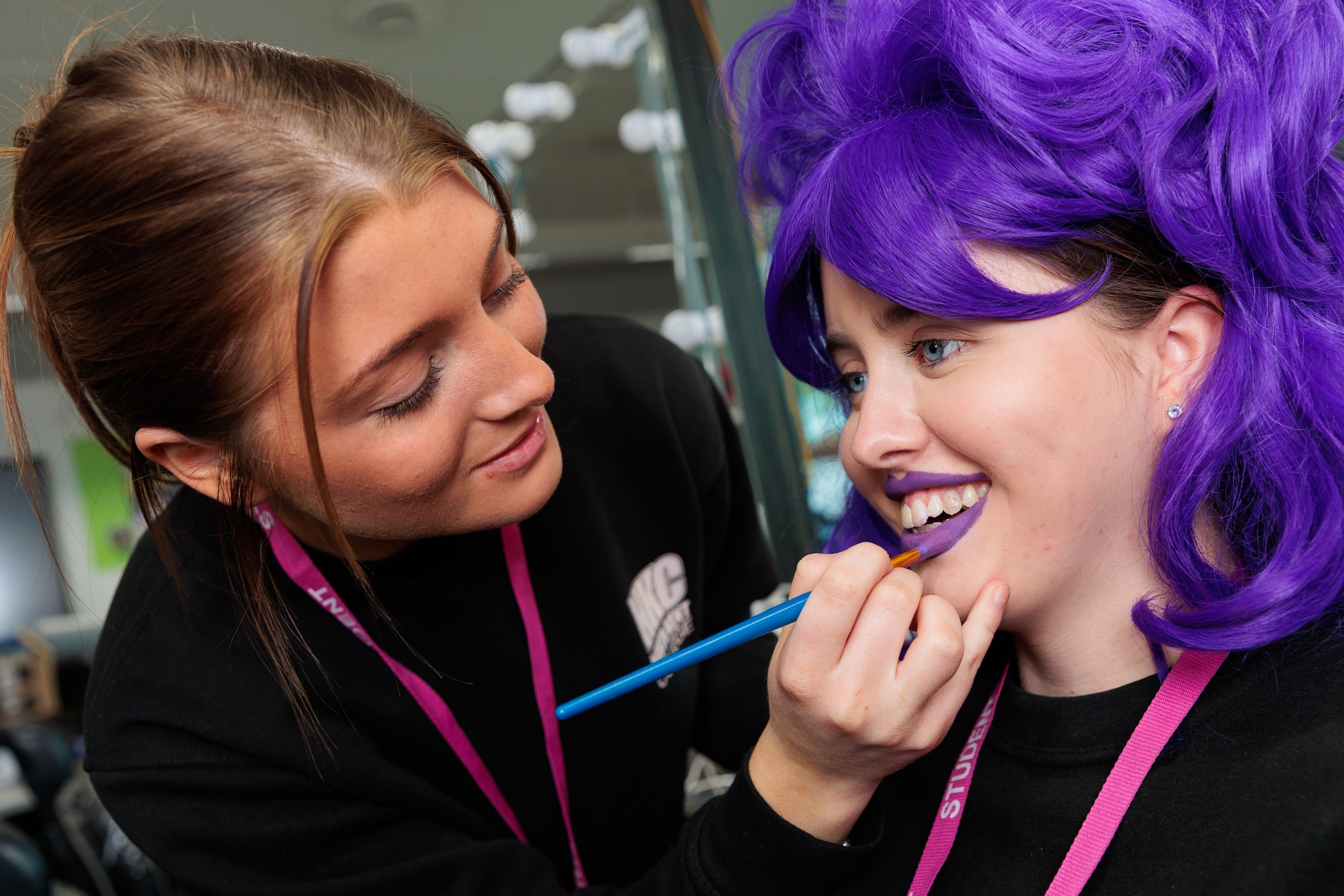 Student applying lipstick to another student