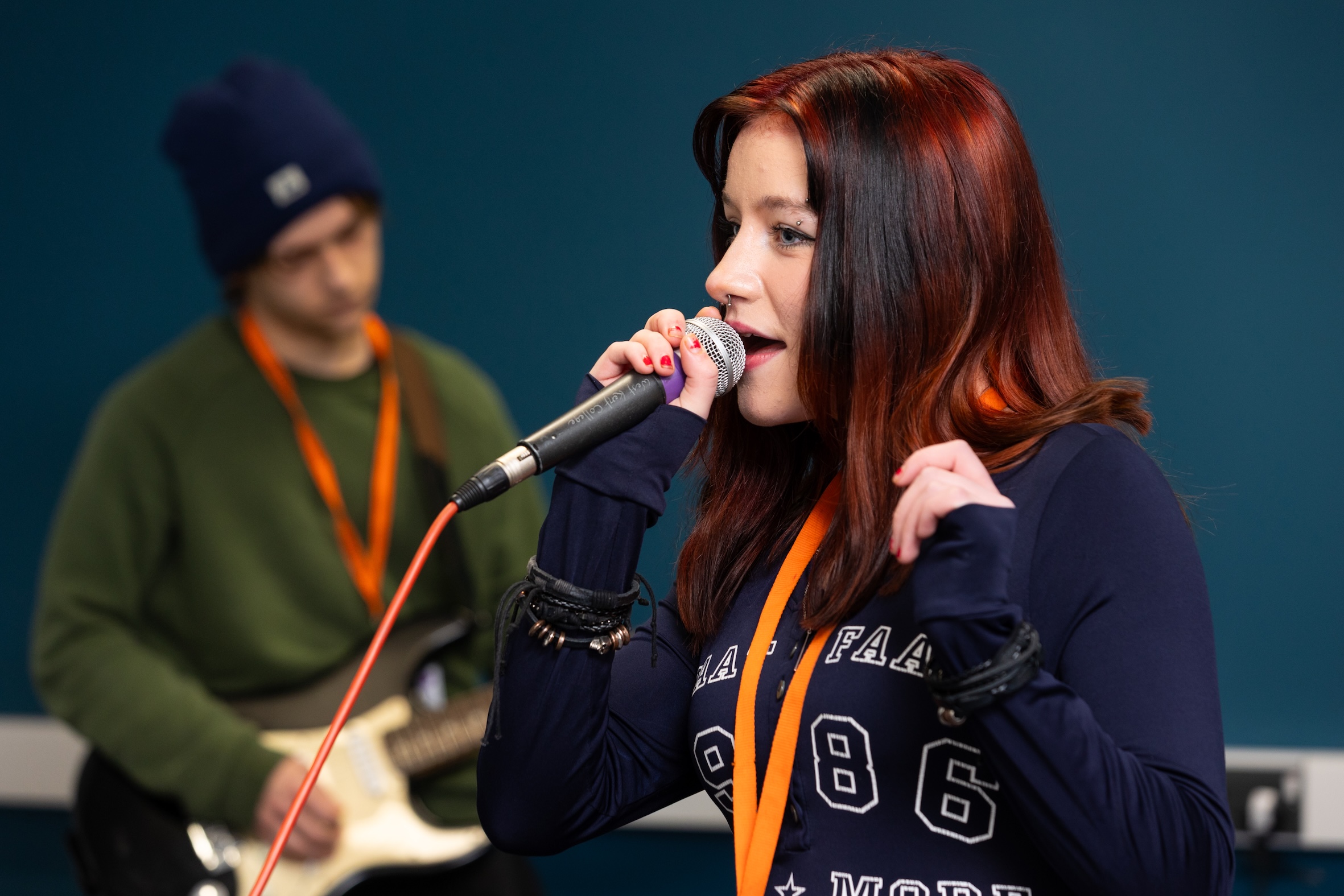 Female student singing into microphone and male student playing guitar in background